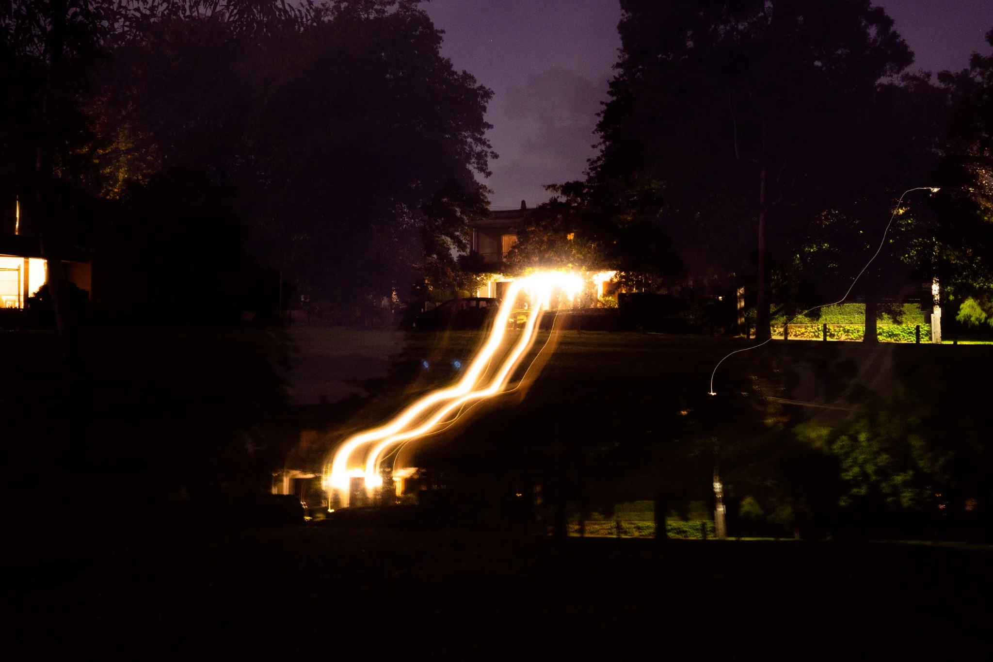 Winding light trail leading toward a lit house